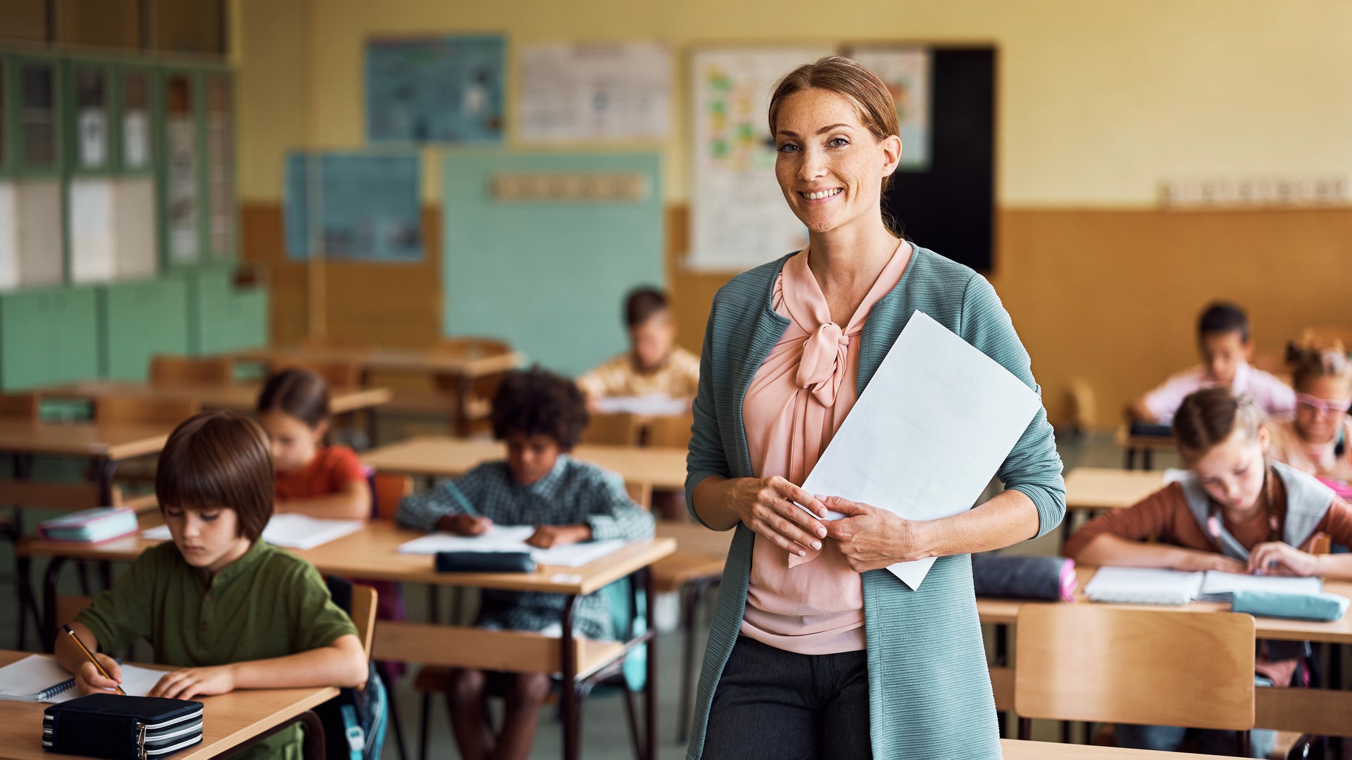 Eine Lehrerin steht lächelnd vor einer Klasse