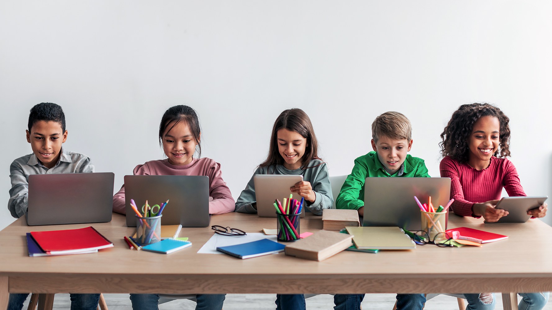 Multiethnische Kinder sitzen an einem Tisch vor Laptops