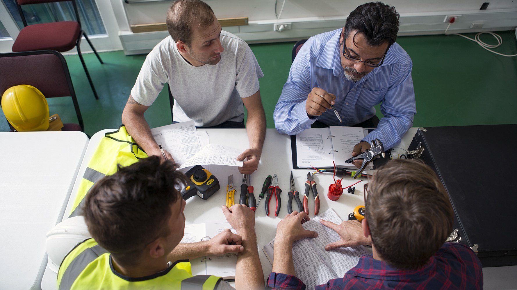 Handwerker mit diversen Werkzeugen sitzen gemeinsam an einem Tisch